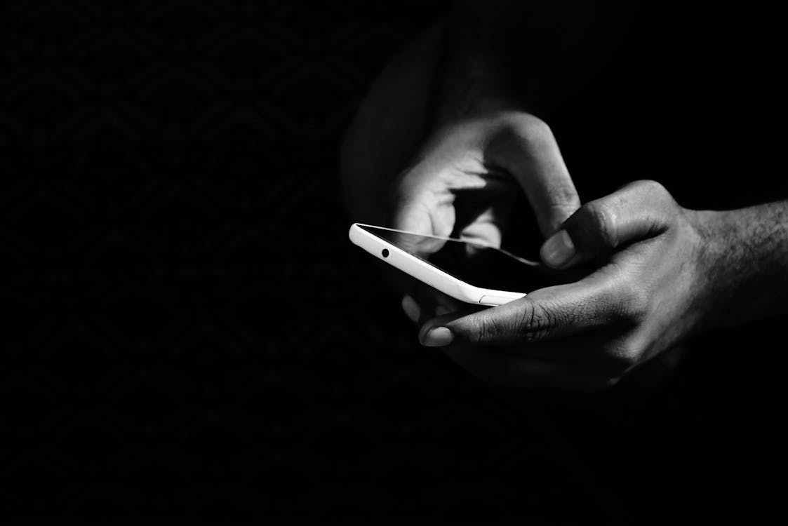 A person holding a smartphone in a black background.